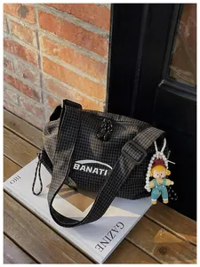 Close-up of a black checkered canvas crossbody bag featuring a BANATI logo and doll charm