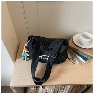 Close-up of black grid canvas shoulder bag with decorative doll charm on a shelf