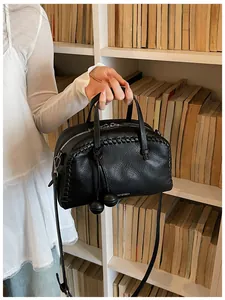 Chic black pebbled leather Boston bag with woven edges and tassels held in a lifestyle setting.