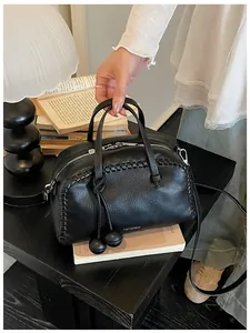 Close-up of black pebbled leather Boston bag with woven edges and decorative tassels.