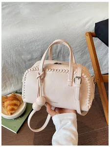 Detail view of a light pink pebble-leather Boston bag with whipstitch trim and charms.