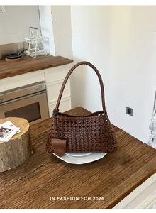 Détail du sac seau à bandoulière tressé marron sur une table en bois dans une cuisine