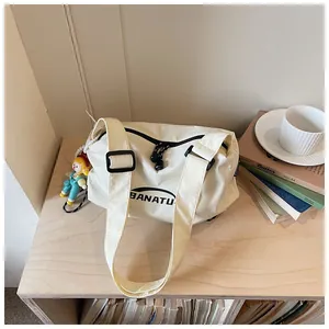 Cream nylon shoulder bag with black 'BANATU' text and cute doll pendant on shelf