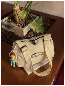 Detail view of cream ripstop canvas shoulder bag featuring cute doll keychain accessory.
