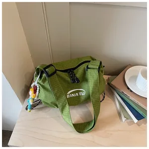 Green checkered canvas shoulder bag with white logo and cute doll charm for daily commute.