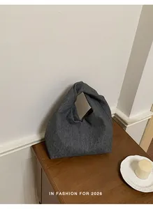 Makrodetail einer grauen, gefalteten Stoff-Tasche auf einem rustikalen Holztisch.