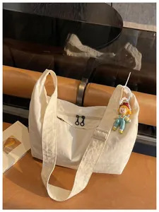 Detail van crèmekleurige nylon crossbodytas met ritszakken en een schattig poppenhangertje.