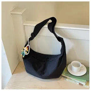 Zwarte nylon hobo schoudertas hangend aan een witte reling in een knusse woonomgeving