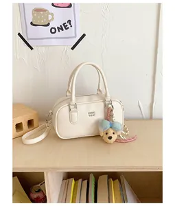 Detailed view of a white pebble-grained bowler bag with cute dog charm on a wooden shelf