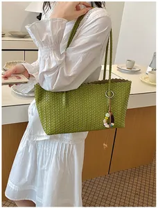 Détail d'un sac à main tissé vert élégant avec un pendentif en perles colorées.