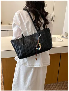 Détail d'un sac cabas noir tressé porté par un mannequin dans une tenue blanche élégante
