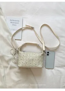 Close-up view of beige plaid handbag featuring rhinestones and a pearl bow charm accessory