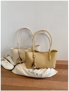 Deux sacs cabas tressés beige et blanc présentés avec des baskets sur un sol en bois