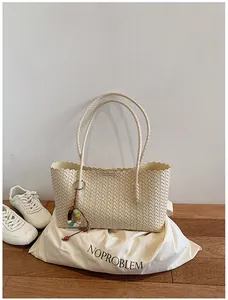Détail d'un sac cabas tressé crème avec perles décoratives sur un fond minimaliste