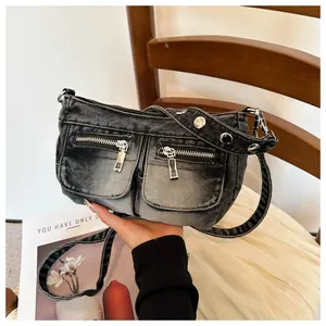 Close-up of black denim crossbody bag with dual front zipper pockets and studs.