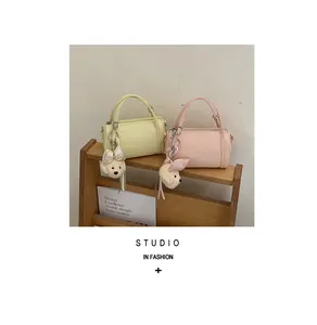Fashionable pastel cylindrical pillow bags with cute plush charms on a wooden shelf