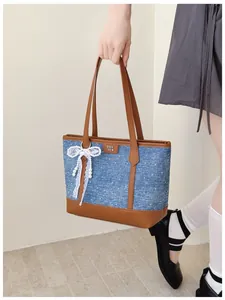 Stylish denim tote bag featuring brown leather trim and a white lace pearl bow detail.