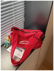 Red checkered canvas crossbody bag with white logo and a cute doll charm detail.