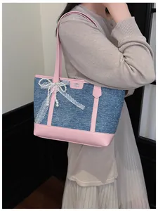 Detail of denim tote bag with pink leather trim, lace bow, and pearls on model.