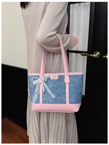 Detailed view of a denim tote bag with pink leather trim and an elegant lace pearl bow