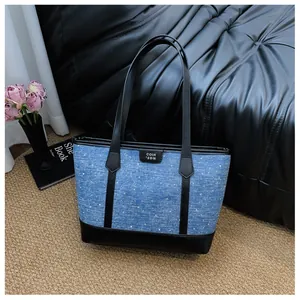 Detailed close-up view of a blue denim tote bag with black leather straps and trim.