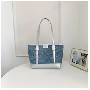 A front-view detail of a stylish denim tote bag featuring silver metallic accents and handles.