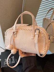 Elegant light pink Boston handbag with woven edge details and decorative pom-poms