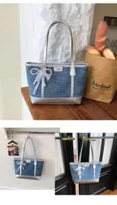 Detail of blue denim tote bag with silver straps and decorative pearl lace bow