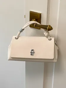 Elegante cremefarbene Kunstledertasche mit Knotengriff an einem Türgriff hängend