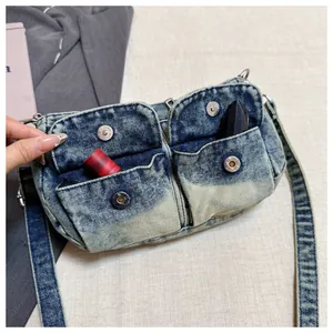 Macro detail view of a washed blue denim crossbody bag featuring functional front pockets