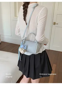 Light blue cylindrical pillow bag with fuzzy charm shown worn over the shoulder