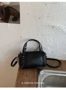 Detail of a black cylinder handbag placed on a wooden table against a rustic white wall.