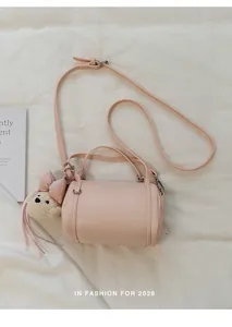 Close-up view of a pink cylindrical crossbody bag featuring a cute teddy bear charm