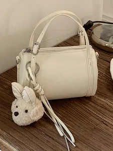 Cream white cylindrical pillow bag with a plush dog keychain on a wooden table.