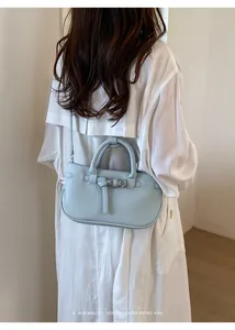 Close-up view of a light blue textured leather crossbody bag styled with a white dress