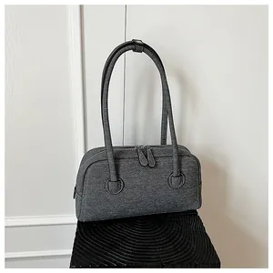 Detailed view of a grey denim-textured Boston bag placed on a black decorative pedestal.