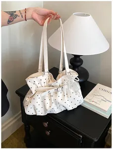 White polka dot pleated tote bag with lace pearl charm accessory on black table.