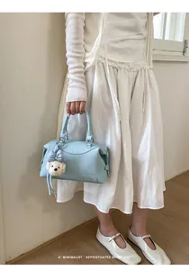 Model holding light blue Boston style handbag with a cute white dog plush charm accessory