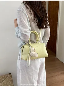 Side view of a pale yellow Boston bag being worn as a crossbody by a model indoors.