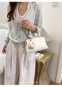 Elegant white Boston handbag with pompom charm in a minimalist indoor lifestyle setting