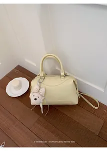 Sophisticated cream Boston handbag with cute plush dog charm on wooden floor background