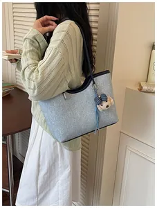 Model trägt eine große hellblaue Jeans-Einkaufstasche mit süßem Bären-Charm-Anhänger