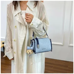 Detail of light blue denim shoulder bag with dark blue trim and teddy bear charm