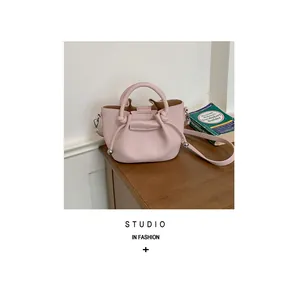 Elegant pink pebbled leather bucket bag on wooden table with shoulder strap