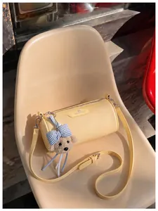 Trendy yellow cylindrical crossbody bag with plush bear charm and adjustable strap