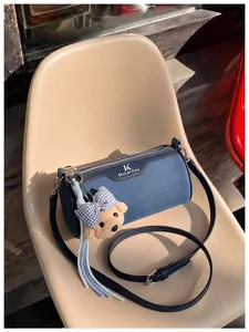 Stylish blue denim cylinder crossbody bag featuring a cute teddy bear charm on a chair