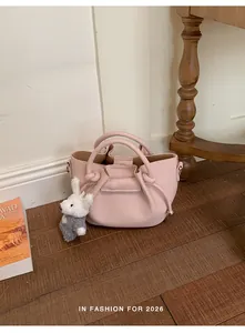 Close-up of a pink leather bucket handbag with a plush bunny charm on wooden floor