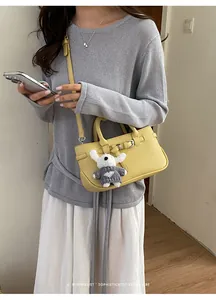 Detailed view of a minimalist yellow leather crossbody bag with a cute dog charm accessory