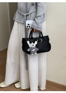 Detail of a chic black pebbled leather handbag featuring a cute white rabbit plush charm
