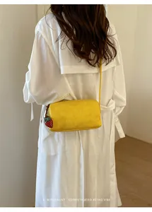 Close-up detail of a minimalist yellow pillow bag with strawberry charm worn as a crossbody